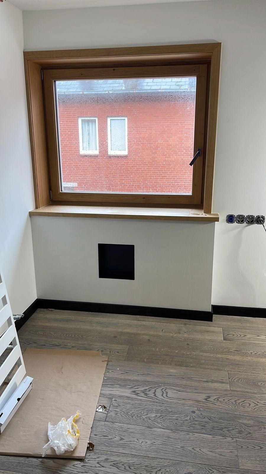 Innenraum mit neu verlegtem Parkettboden, großem Holzfensterrahmen und roher Wandöffnung für Installationen