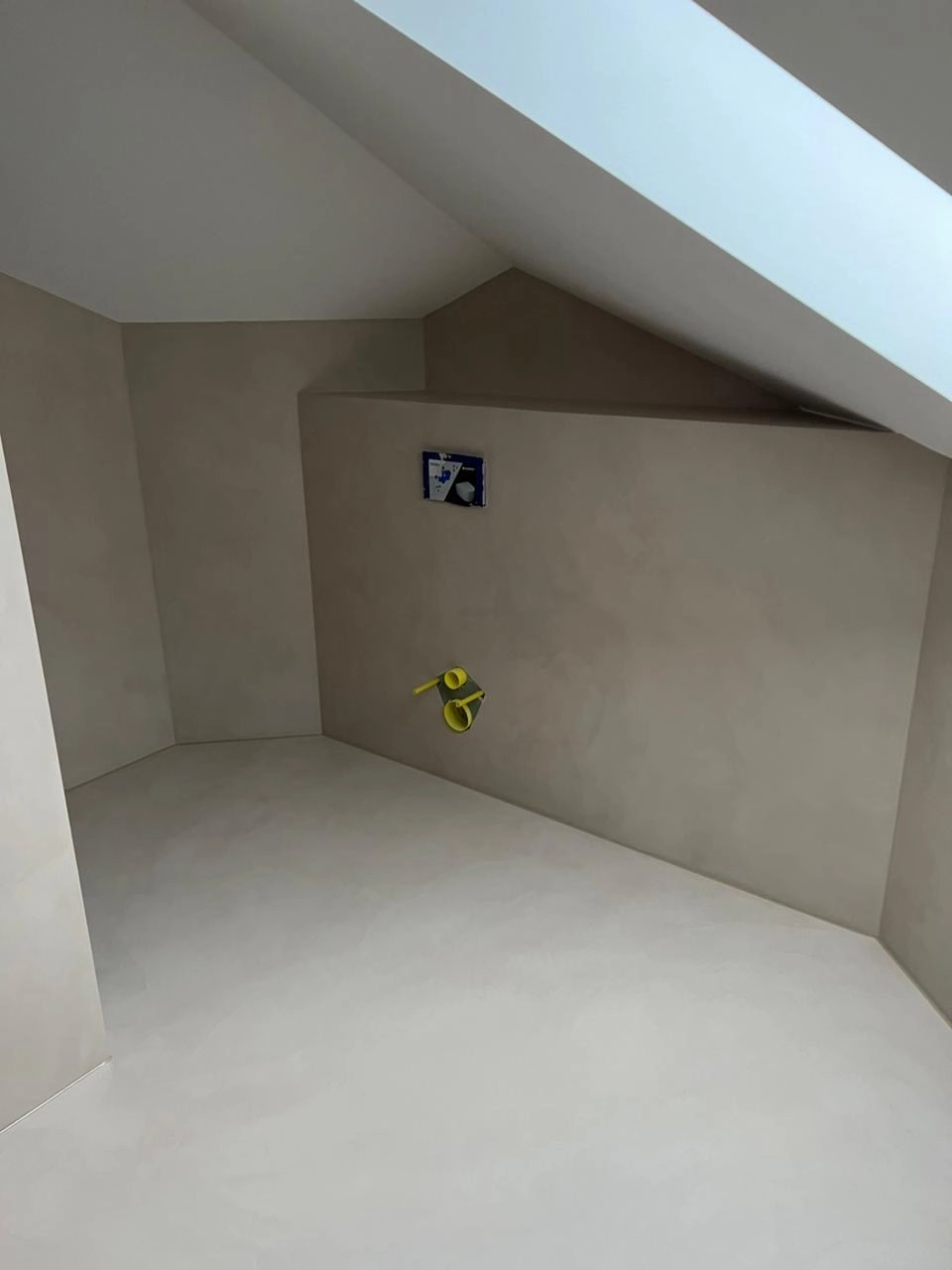 Raum mit grauem Mikrozementboden und -wänden sowie vorbereitetem Wand-WC-Anschluss