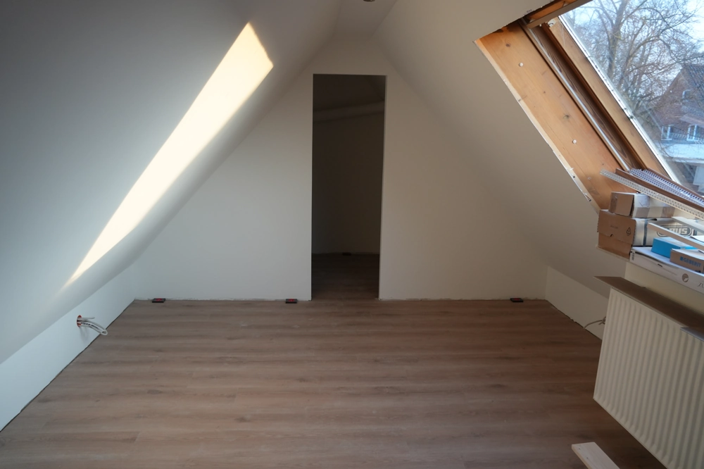 Dachgeschossausbau: heller Spitzboden mit weiß verputzten Wänden, neu verlegtem Laminatboden und Dachfenster