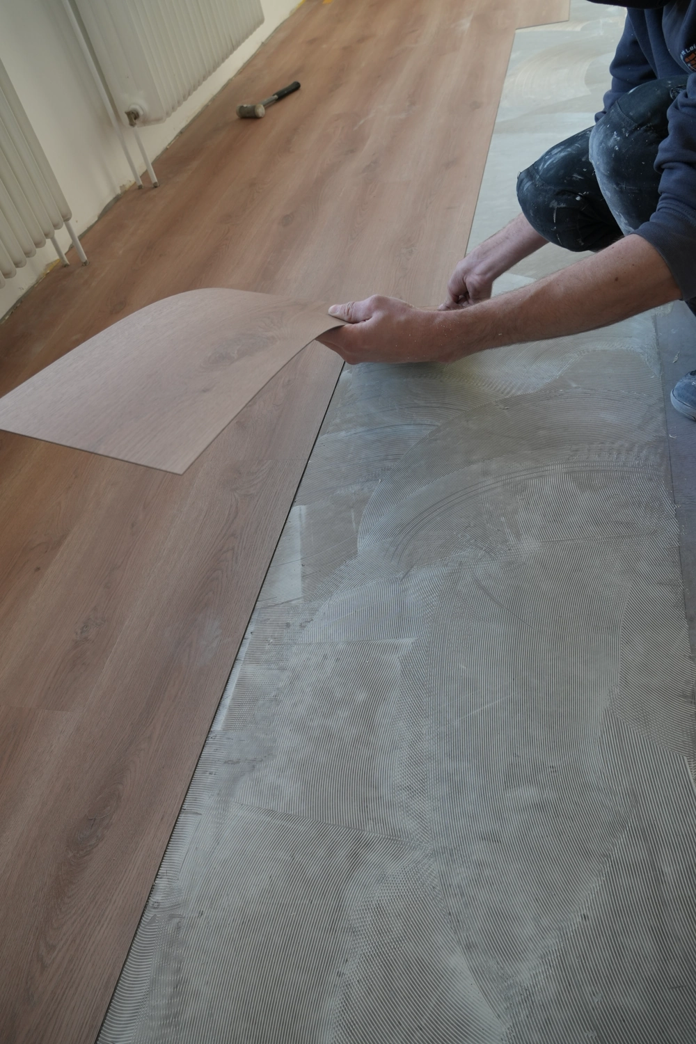 Vinylboden verlegen: Arbeiter setzt Vinyldiele auf vorbereiteten Estrich