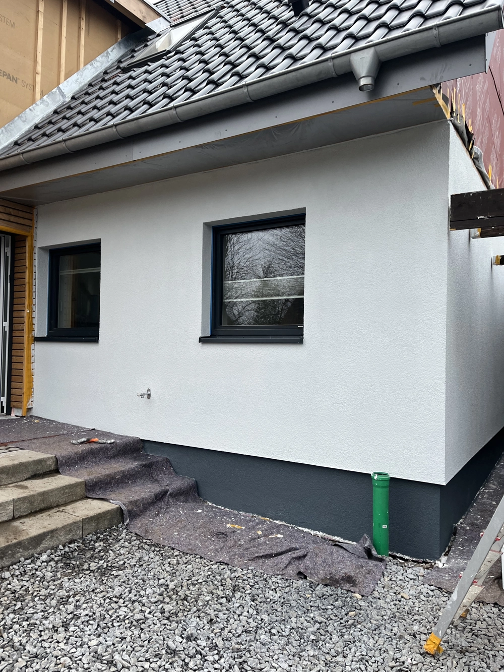 Frisch verputzte Fassade mit grauem Sockel und zwei neuen Fenstern im Rahmen der Fassadensanierung