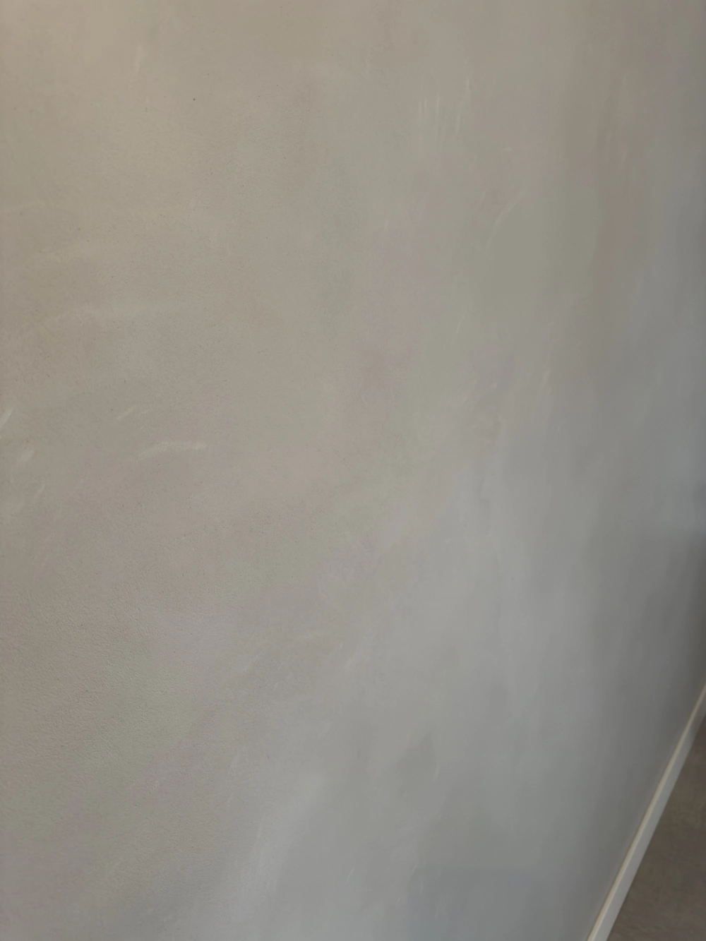Verputzte Innenwand Putzarbeiten mit glatter hellgrauer Oberfläche und weißer Sockelleiste