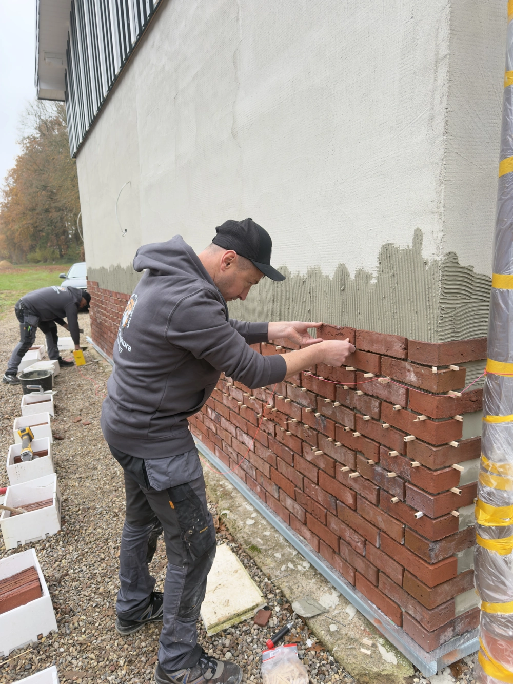 Handwerker bringen rote Klinkerriemchen an einer Hausfassade an