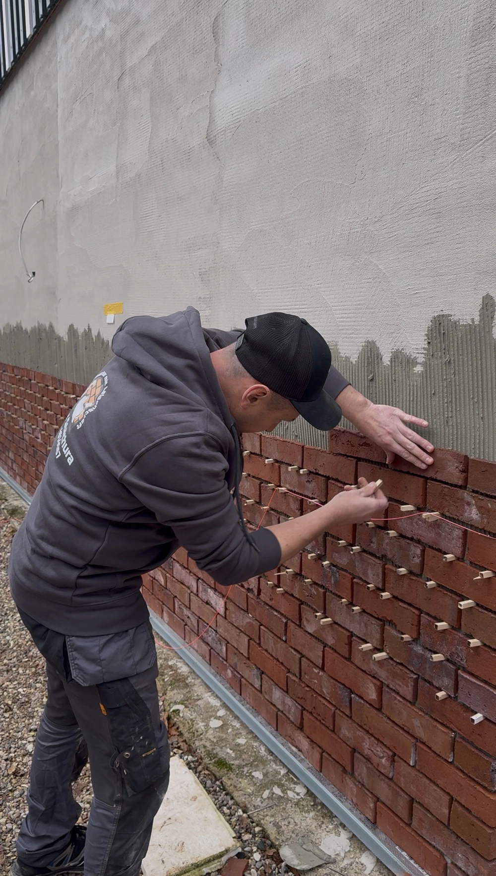 Handwerker bringt rote Klinkerriemchen mit Abstandshaltern präzise an Außenwand an