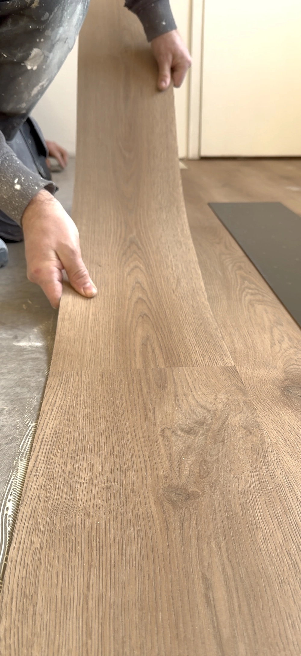Hand eines Monteurs verlegt Vinylboden in Holzoptik auf Untergrund