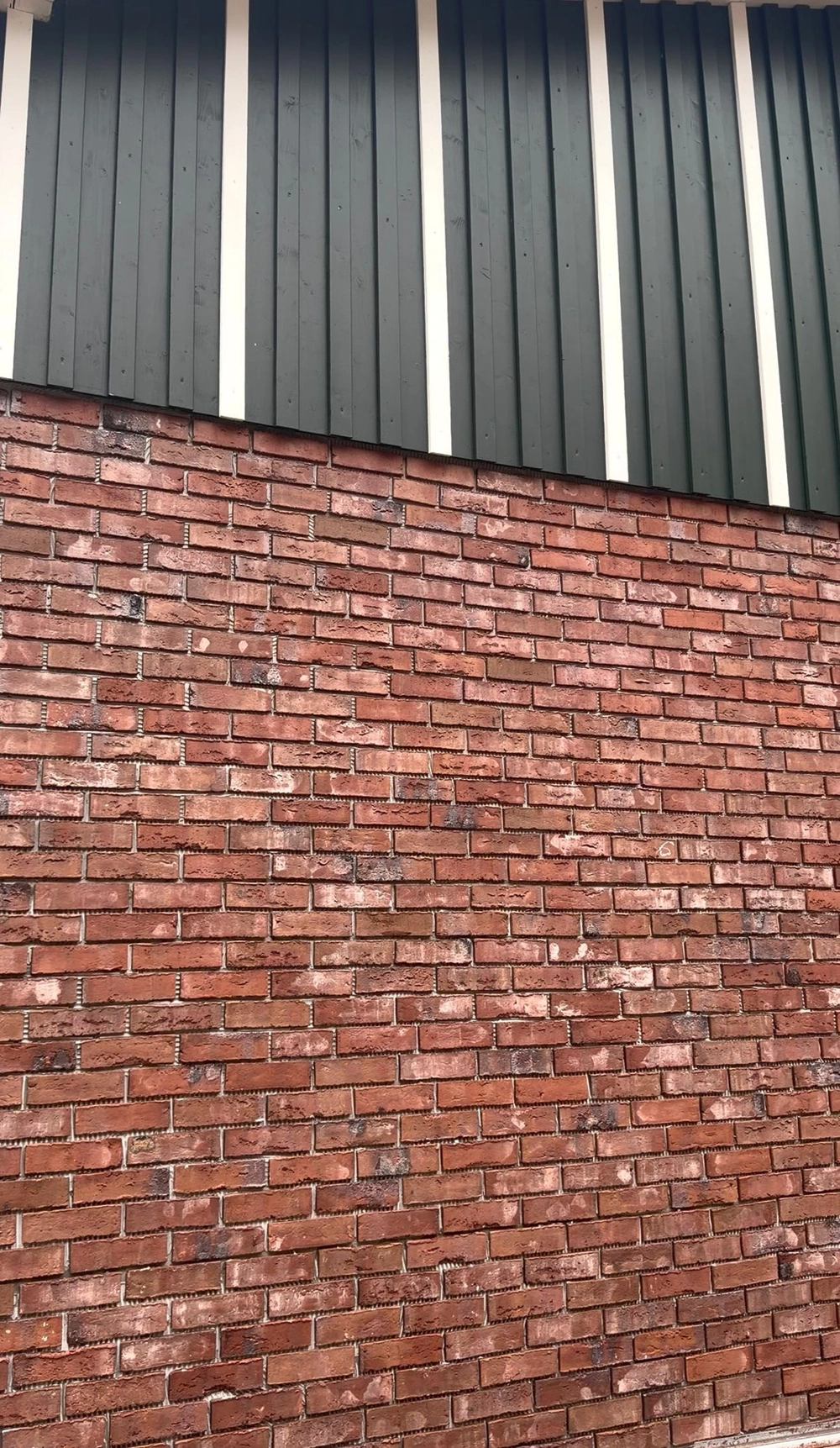 Fassade mit grünen Metallpaneelen und rotem Klinkerriemchen