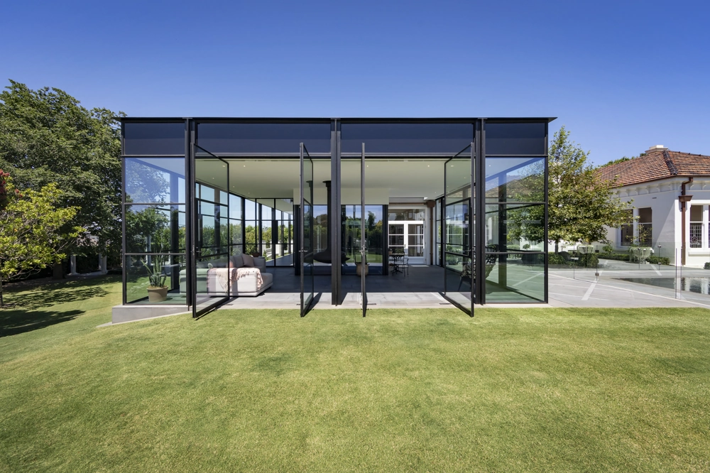 Moderner Gartenpavillon mit bodentiefen Glasschiebetüren und schwarzem Stahlrahmen auf Rasenfläche