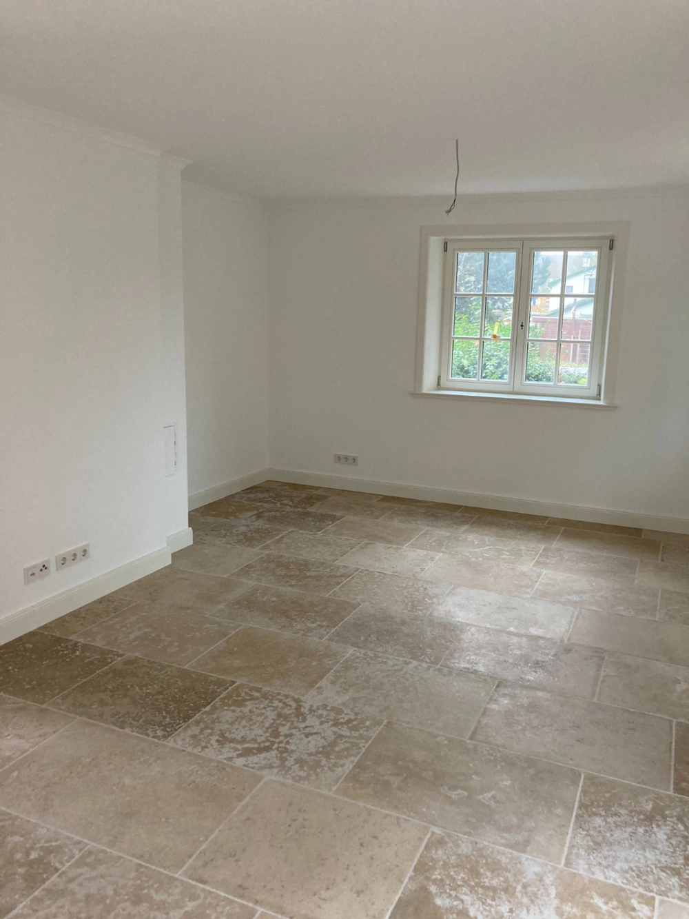 Heller Wohnraum mit Naturstein-Bodenbelägen, frisch verlegten großformatigen Fliesen und weiß verputzten Wänden