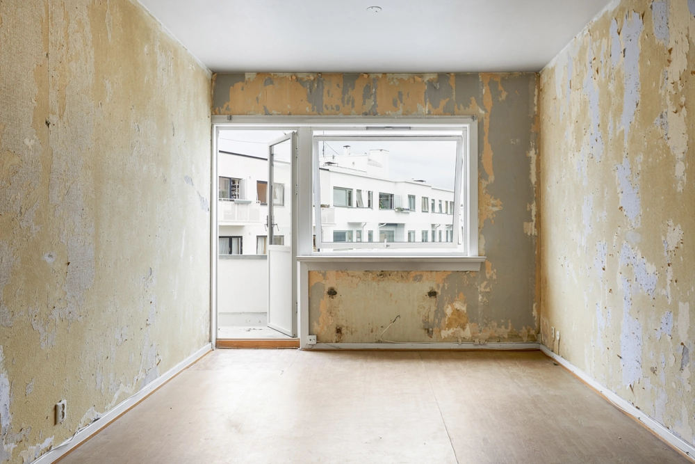 Leerer Raum mit abgeplatztem Putz und rohem Fußboden vor Demontagearbeiten