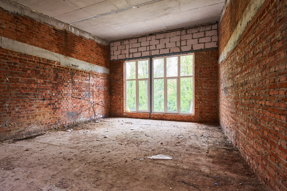 Unfertiger Raum mit freigelegten Ziegelwänden und staubigem Boden vor Abbrucharbeiten