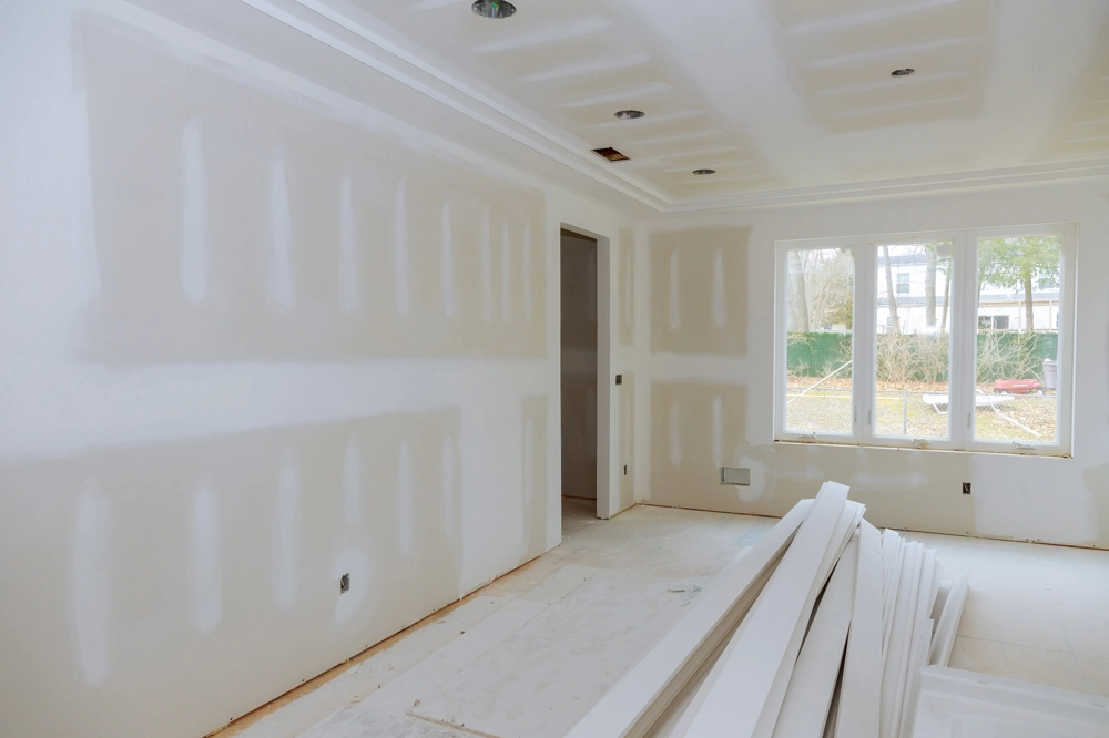 Trockenbauarbeiten in Innenraum mit gespachtelten Gipskartonwänden, abgehängter Decke und gestapelten Platten auf dem Boden