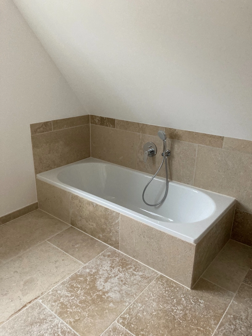 Badewanneneinbau mit beigefarbenen Natursteinfliesen im Rahmen einer Badsanierung