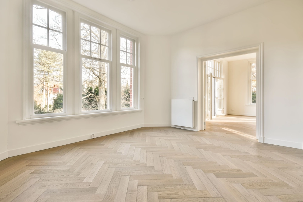 Leerer, lichtdurchfluteter Raum mit großen Fenstern, weißen Wänden und Fischgrät-Eichenparkett nach Parkett verlegen