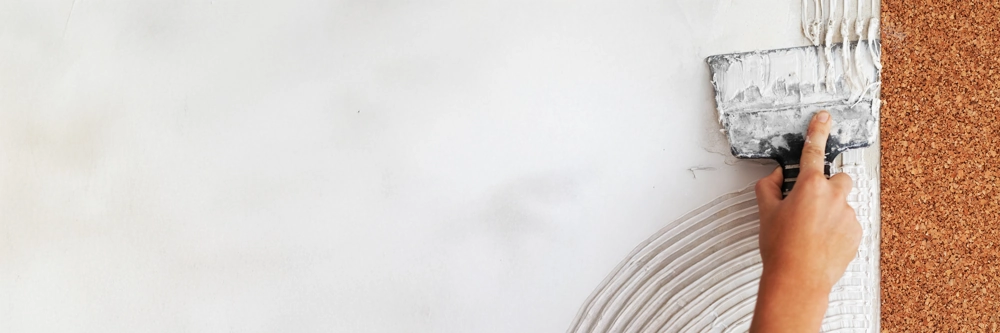 Hand streicht Weißputz mit Zahnspachtel auf Korkdämmplatte an Fassade – Putzarbeiten