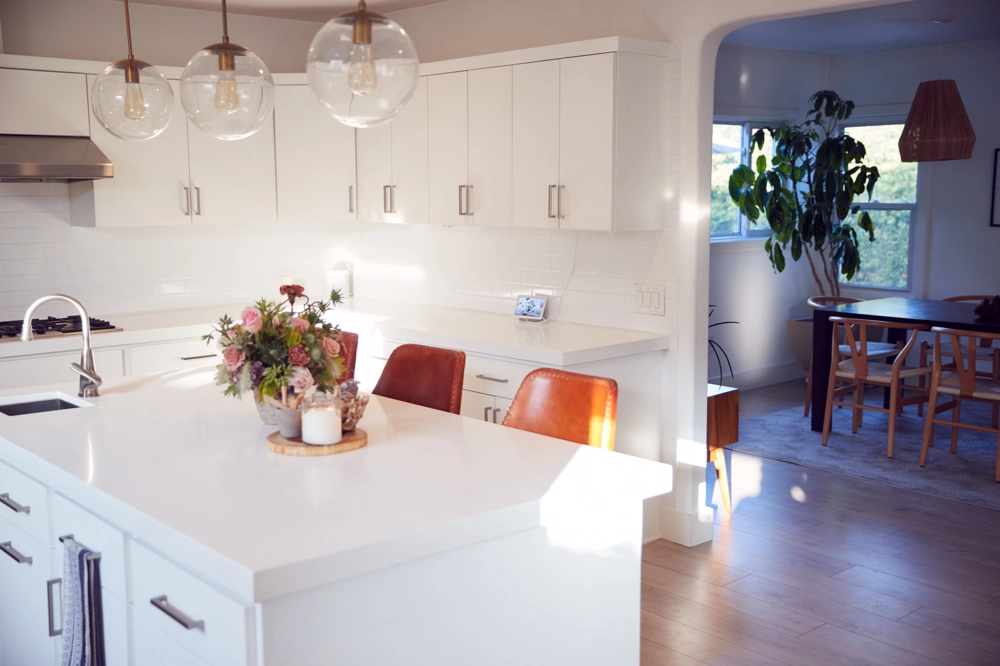 Weiße Kücheninsel mit Blumenbouquet, Leder-Barhockern und Parkettboden nach Küchenrenovierung