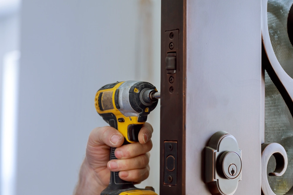 Hand mit Akku-Schrauber montiert Türschloss und Scharnier an einer Innentür bei Türmontage