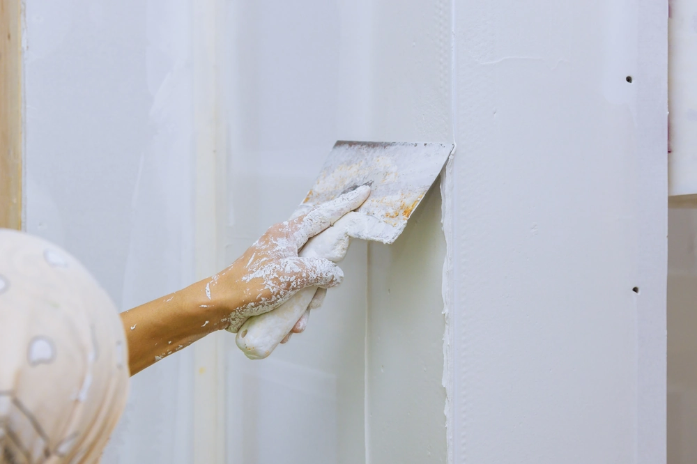 Hand mit Glättkelle glättet Spachtelmasse auf Gipskartonwand für Spachtelarbeiten