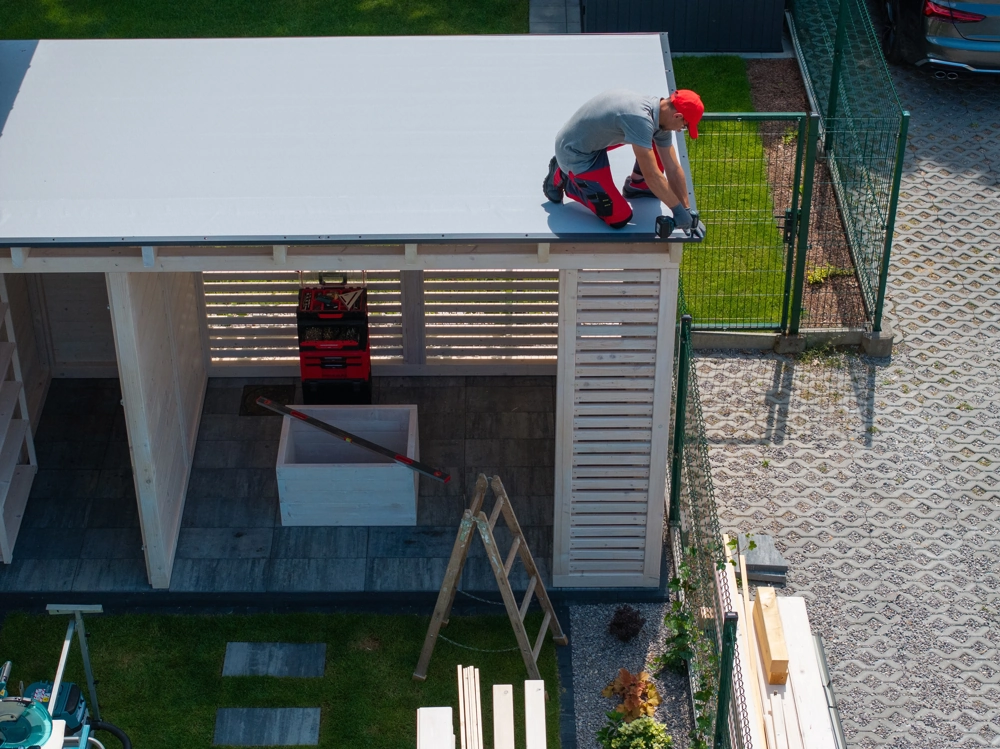 Handwerker montiert Dach eines freistehenden Holz-Gartenpavillons im Garten unter Nutzung von Werkzeug und Leiter