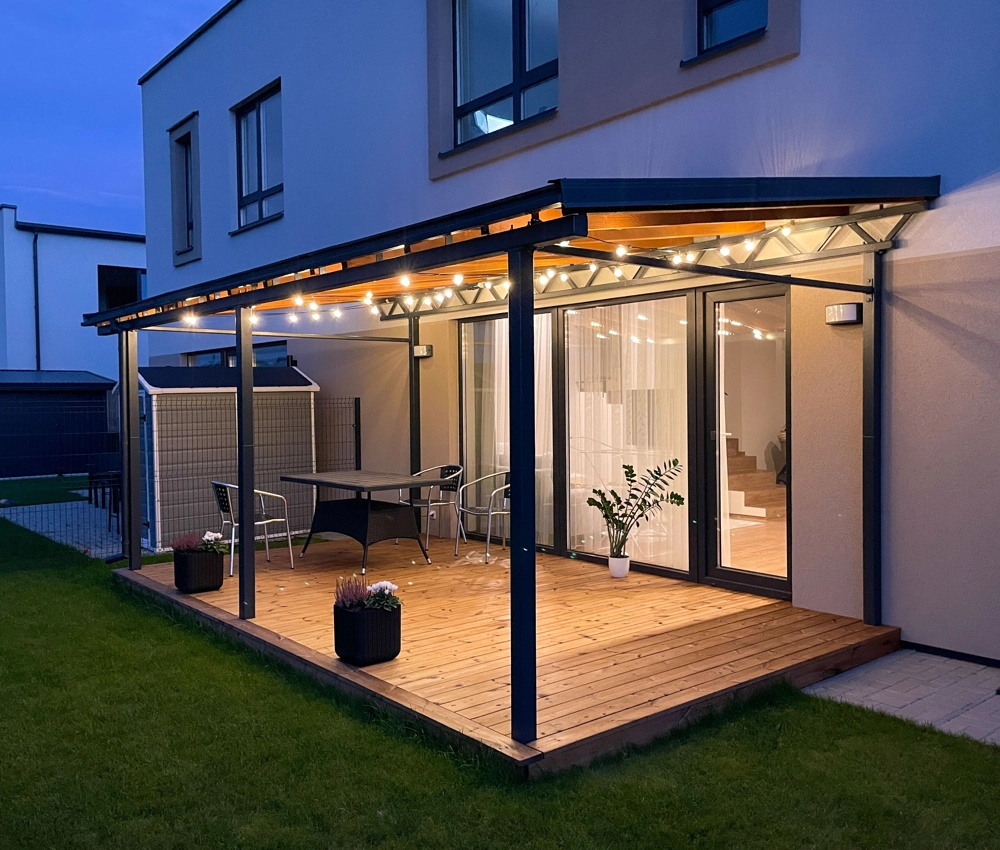 Terrassenüberdachung mit Holzboden, Metallstützen und LED-Beleuchtung vor bodentiefen Fenstern