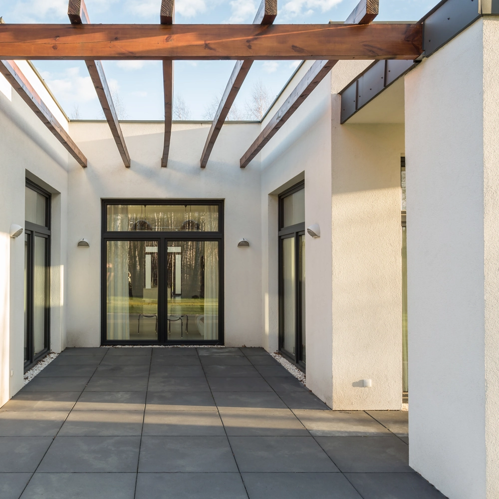 Pergola mit großformatigen Terrassenplatten und weißen Hauswänden