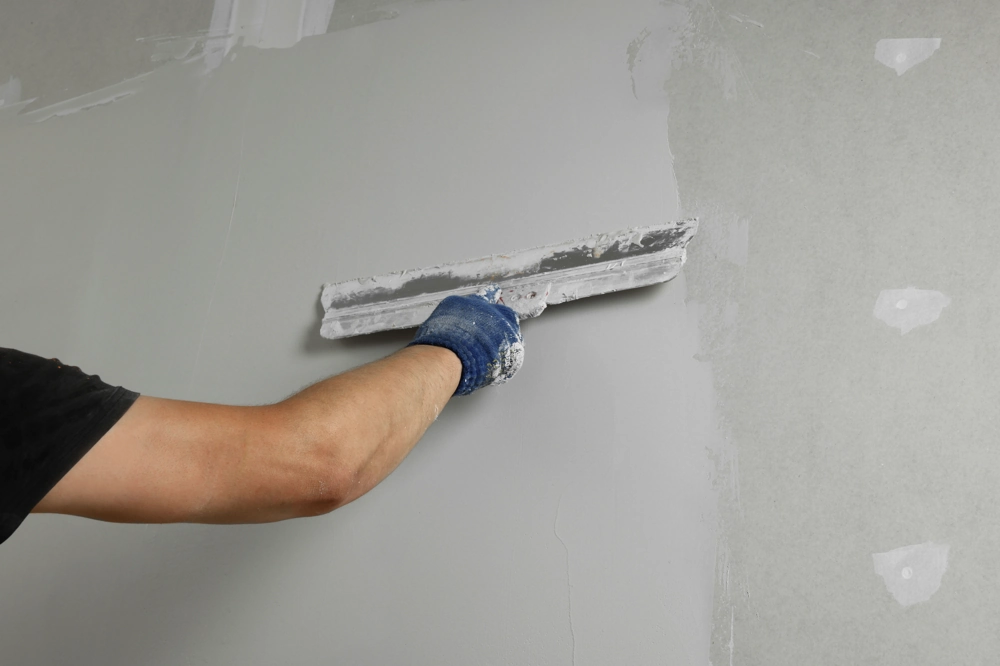 Handwerker glättet Wand mit Glättspachtel bei Spachtelarbeiten
