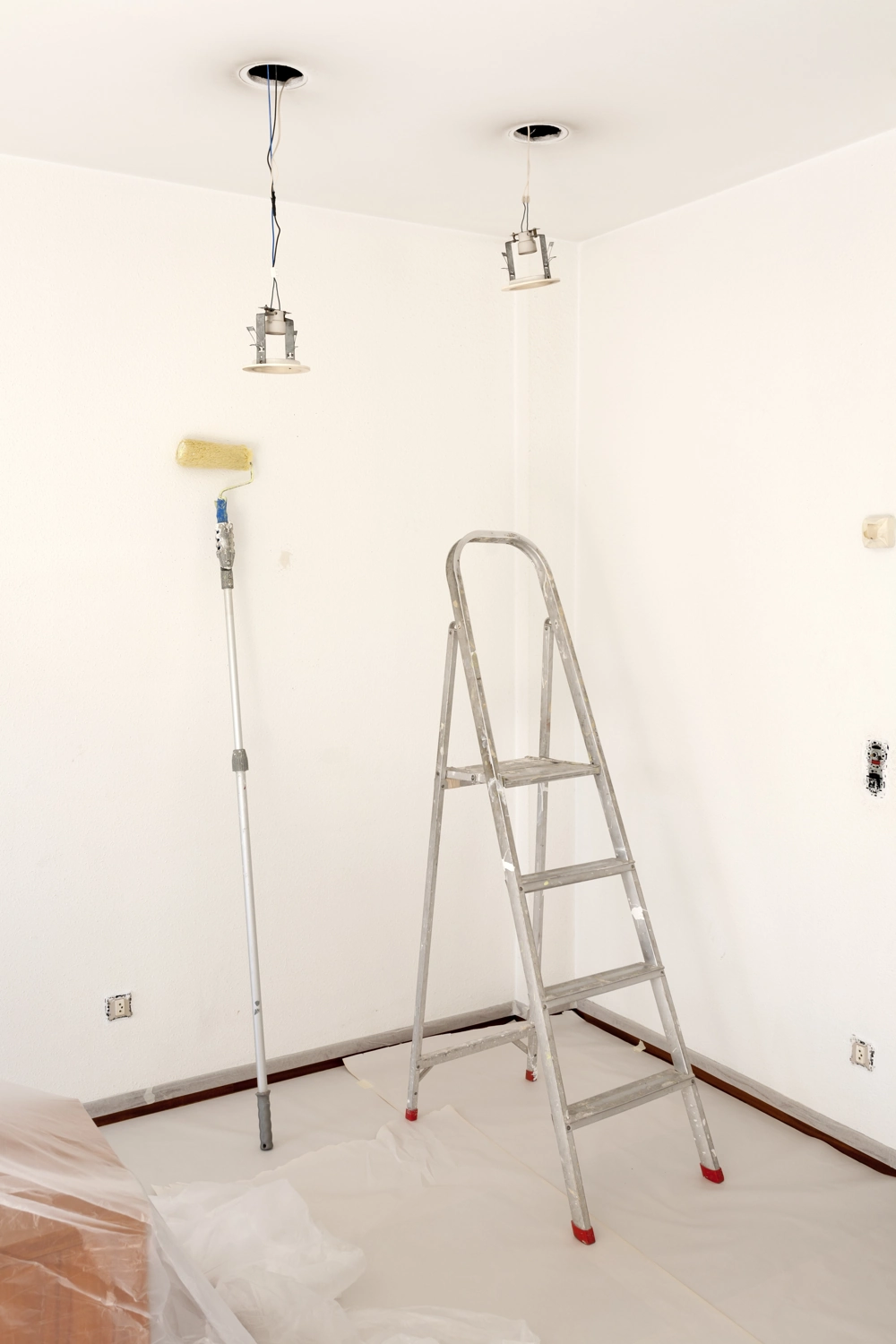 Leiter und Farbroller in weißem Raum bei laufenden Malerarbeiten und Installation von Deckenleuchten