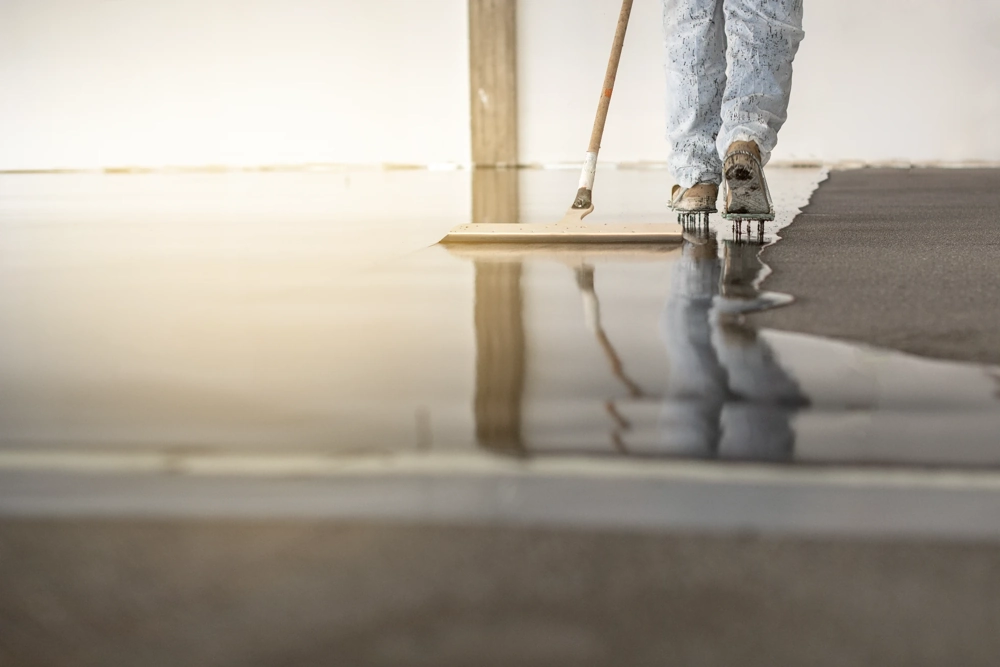 Handwerker mit Spikeschuhen verteilt selbstnivellierenden Estrich auf rohem Untergrund im Innenbereich