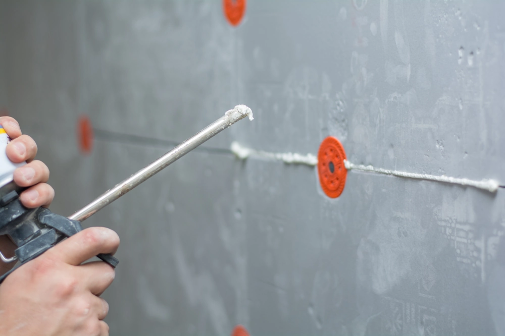 Auftragen von Montageschaum in die Fugen grauer Dämmplatten mit Befestigungsdübeln im WDVS