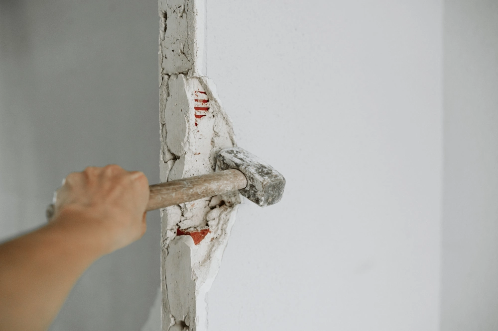 Hand mit Vorschlaghammer entfernt Putz an Innenwand im Rahmen von Abbrucharbeiten