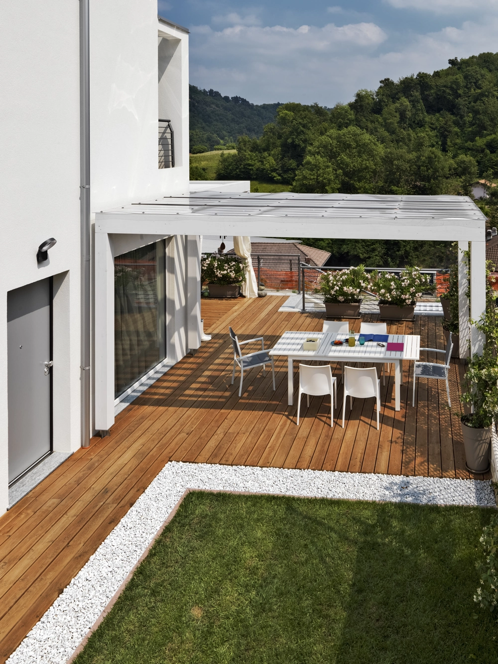 Terrassenüberdachung aus weißer Konstruktion über Holzdielen mit Gartenmöbeln auf gepflegter Dachterrasse